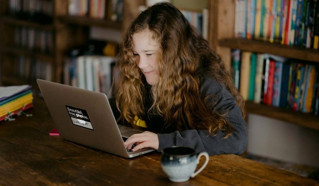 A young person studying with a laptop beside books at home